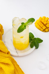 Refreshing drink with mango pulp and mint in a glass with a glass straw on the white background, cut mango next to the glass
