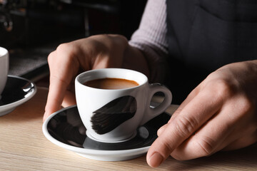 Barista with cup of fresh aromatic coffee at wooden counter in cafe, closeup