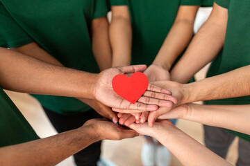 charity, support and volunteering concept - close up of volunteers's hands holding red heart at distribution or refugee assistance center - obrazy, fototapety, plakaty