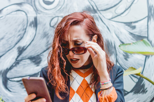 Young Business Woman Squinting And Confused Looking At Her Mobile Screen With Concern.