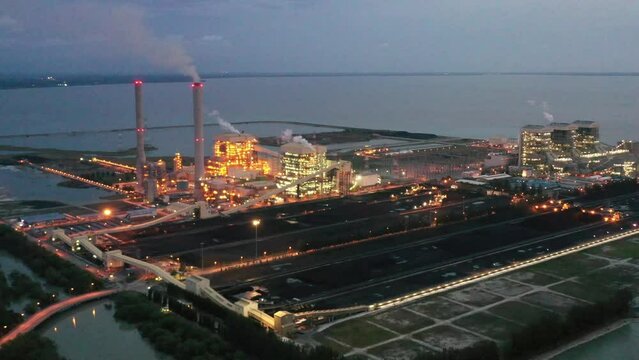 At dusk drone fly around ultra-supercritical coal-fired power plant by Tenaga Nasional Berhad TNB located at artificial island, manjung, perak, malaysia, illuminated industrial power station.