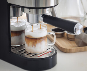 A clear glass cup of dirty coffee latte while espresso machine maker brewing and pouring hot, fresh...