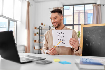 distance education, primary school and remote job concept - happy smiling male math teacher with laptop and simple mathematical equalities having online class at home office