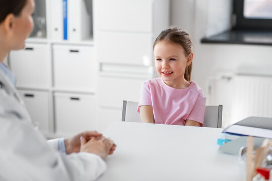 Medicine, Healthcare And Pediatry Concept - Female Doctor Or Pediatrician Talking To Happy Smiling Little Girl Patient On Medical Exam At Clinic