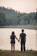 Fototapeta premium The scenery of a couple holding hands together at the lake at sunset time.