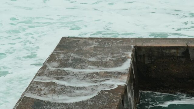 Close-up of sea waves breaking on stone breakwater. White sea foam bubbles on the surface of the water. Dramatic sea on a gray cloudy day. Marine patterns. Beautiful waves in a storm.