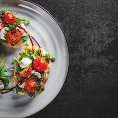Italian bruschetta with roasted tomatoes, mozzarella cheese, balsamic vinegar and herbs on plate on Dark grey black slate background