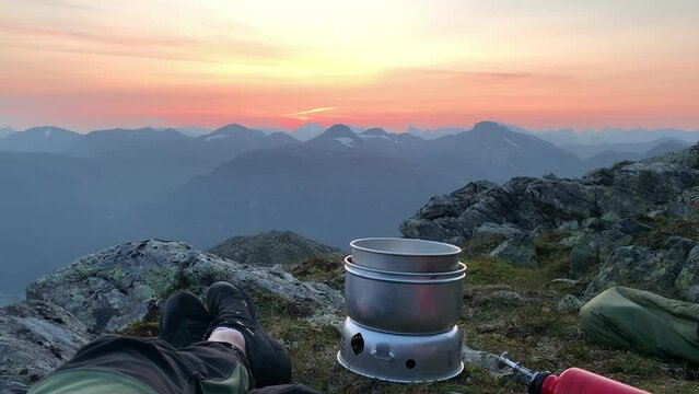 Norwegian hiker crossing feet laying on mountain top in midnight sun sunset - pov