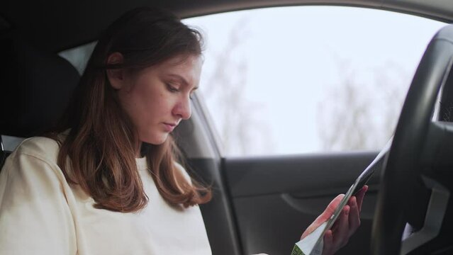 Young female driver holds a map in her hands and chooses the direction for the trip. Navigating the terrain with a paper map 4K 10 BIT