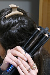 Fototapeta premium Mujer usando un rizador de pelo para rizarse el pelo. Pelo de color oscuro. Persona de color blanco.