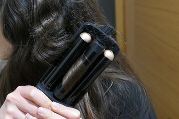 Fototapeta premium Mujer realizando ondas en su pelo negro. Ondulador de pelo
