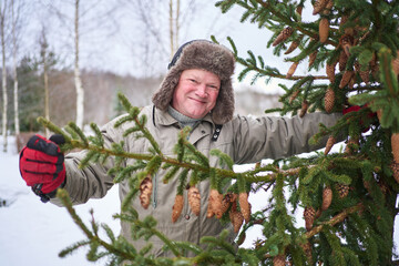 smiling senior man in a hat with earflaps in winter holds a fir branch covered with cones