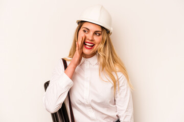 Young architect woman with helmet and holding blueprints isolated on white background shouting and holding palm near opened mouth.