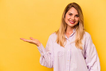 Young caucasian woman isolated on yellow background showing a copy space on a palm and holding...