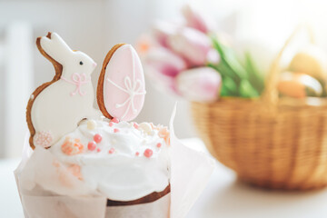 Cookies in the form of rabbit and an egg on an Easter cake in front of basket with tulips.