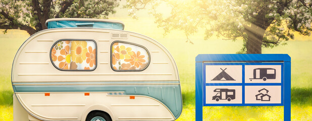 Retro seventies caravan with camp site greeting sign in front of blooming trees with summer sunlight - obrazy, fototapety, plakaty