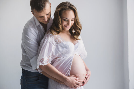 Happy couple in white clothes looks at big pregnant belly. Tenderness romantic atmosphere
