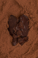 Pieces of craft chocolate on cocoa powder background. Homemade chocolate.