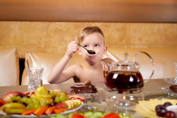A little blond boy without a shirt at a table with tea and fruit in a beautiful room in a Russian bath. The guy eats at the table. The concept of a healthy holiday