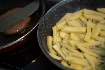 Cooking meat and fries in oily saucepan   