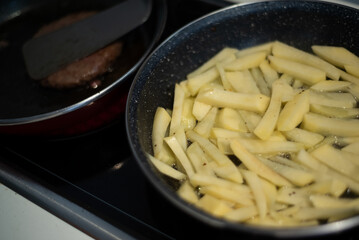 Cooking meat and fries in oily saucepan   