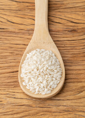 Raw carnaroli risotto rice on a spoon over wooden table