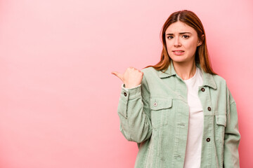 Young caucasian woman isolated on pink background shocked pointing with index fingers to a copy space.