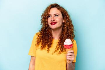 Young ginger woman holding an ice cream isolated on blue background dreaming of achieving goals and purposes