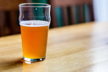 Glass mug of light beer with foam on a wooden table in a cafe close-up