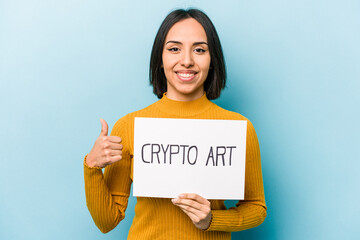 Young hispanic woman holding crypto art placard isolated on blue background smiling and raising...