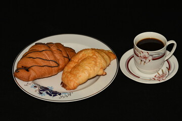 porcelain platter with Croissants, and a cup of coffee on black background
