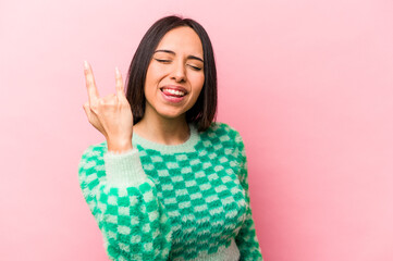 Young hispanic woman isolated on pink background showing rock gesture with fingers