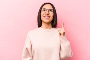Young hispanic woman isolated on pink background indicates with both fore fingers up showing a...