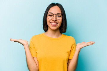 Young hispanic woman isolated on blue background makes scale with arms, feels happy and confident.