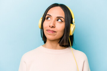Young hispanic woman listening to music isolated on blue background