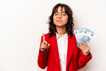 Young business hispanic woman holding banknotes isolated on white background showing number one with finger.