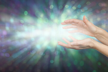 Healer channeling high resonance  Healing Energy - female cupped hands with light between against a green bokeh effect background and space for messages
