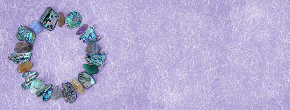 Circular crystal frame message background - tumbled healing stones and paua shell arranged in a neat circle on left side against a fibrous lilac background with space for copy
