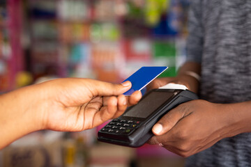Close up shot of customer paying money by tapping credit card to swiping machine at grocery shop -...