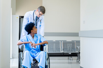 Fototapeta premium A male doctor takes a male patient who is admitted at the hospital for a walk through the window corridors of the hospital for psychotherapy. by having the patient sit in a wheelchair