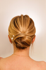 Fototapeta premium The concept of style, style and beauty. An isolated shot of a girl from behind with blonde hair gathered in a neat bun at the back of her head, against a white studio background. A hairstyle for girls