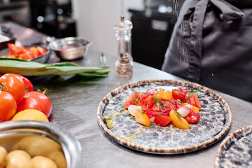 Close-up of dish with fresh vegetable salad on plate on table with chef adding spices
