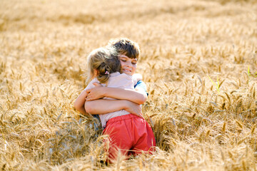 Naklejka na ściany i meble School kid boy and little sister, preschool girl hugging on wheat field. Two happy children playing together and having fun sunny summer day. Siblings in love.