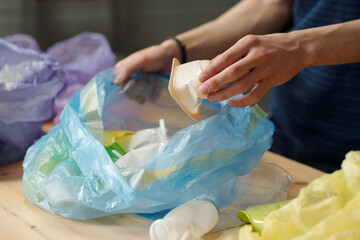Hand of adolescent guy putting white small plastic yoghurt container into cellophane sack with...