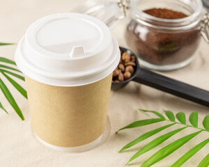 Coffee to go. Disposable eco-friendly cardboard cup, ground coffee in a glass jar on the sand with palm leaves. Takeaway coffee concept. Vacation with coffee