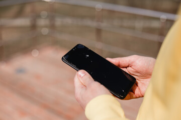 Hands hold a smartphone with cracked glass. The man smashed the screen of the phone. The ideal concept for the design and repair of phones and electronics. Cracked mobile phone glass