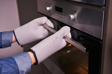female hands in mittens open the oven