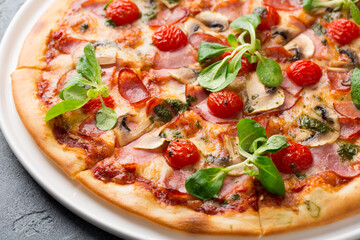 Sliced tasty pizza with mushroom, cheese, tomatoes, pepper, becon, sausage, fresh salad and pesto. Italian pizza