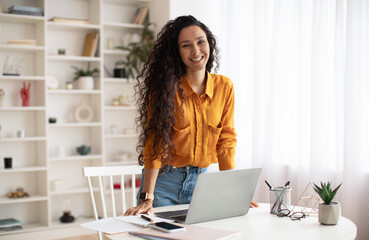 Happy Middle Eastern Female Entrepreneur Standing Near Laptop In Office
