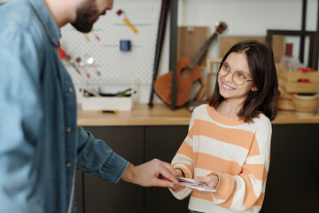 Smiling little girl in eyeglasses and striped casual pullover offering young man choose single card from deck in her hands during leisure game
